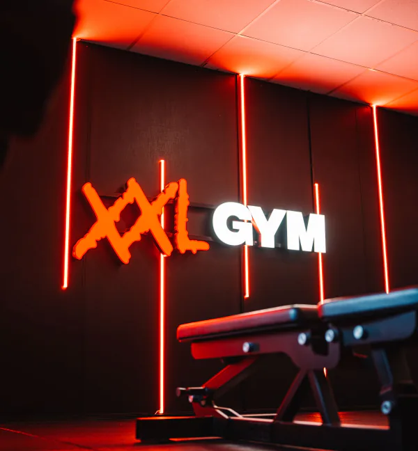 De verlichte XXL Gym-logowand met rode lichtlijnen en een trainingsbank in XXL Gym Nuenen